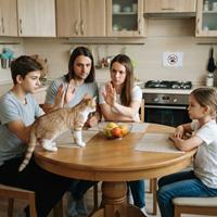 Una familia unida enseña a un gato atigrado a no subir a la mesa de la cocina
